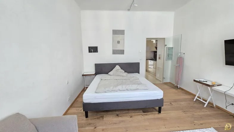 Helles Schlafzimmer mit Holzboden, einem bequemen Bett und Blick in die angrenzende Küche.