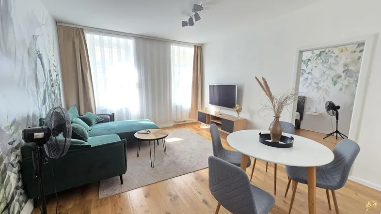 Helles Wohn- und Esszimmer mit modernem Sofa, Esstisch und Holzboden, dekoriert mit Pflanzenmotiven.