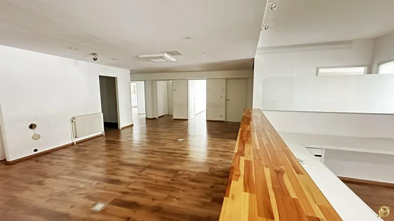Geräumiger, offener Gewerberaum mit Laminatboden und einer Holztheke, bereit zur individuellen Gestaltung.