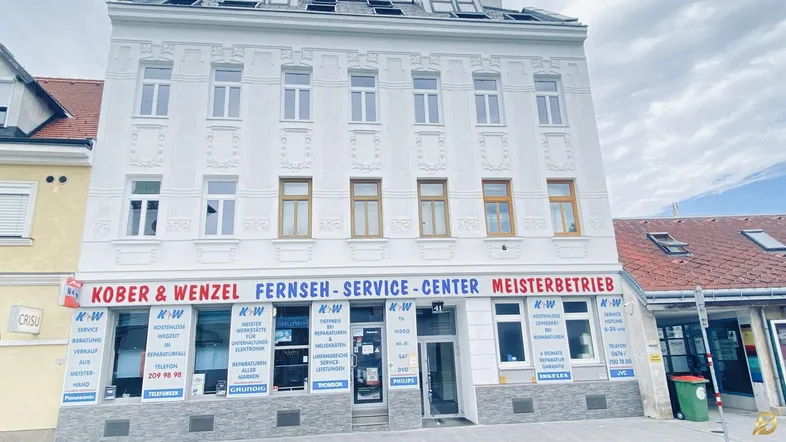 Weißes Mehrfamilienhaus mit Geschäften im Erdgeschoss und vielen Fenstern.