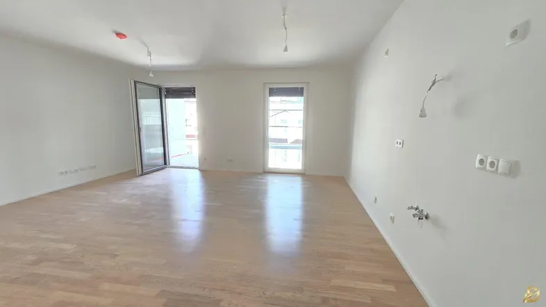 Helles, leeres Zimmer mit Parkettboden und Zugang zu einem Außenbereich, bereit für die Einrichtung.