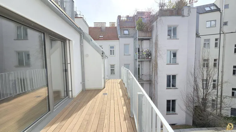 Geräumige Holzterrasse mit Blick auf die umliegenden Gebäude und Glasschiebetüren zum Innenbereich.