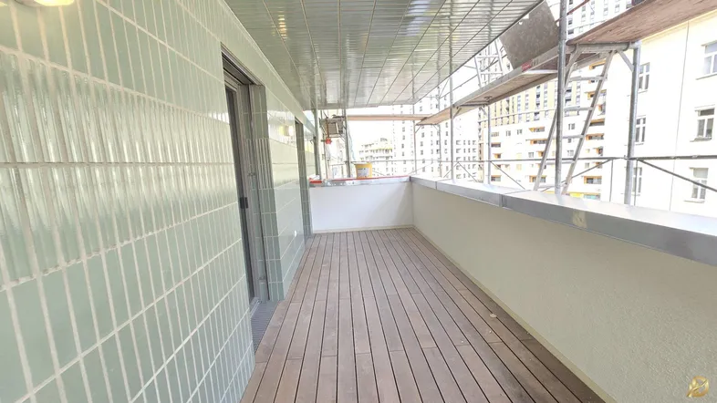 Geräumiger Balkon mit Holzfußboden und modernen Fliesen an der Wand, umgeben von Gerüsten.