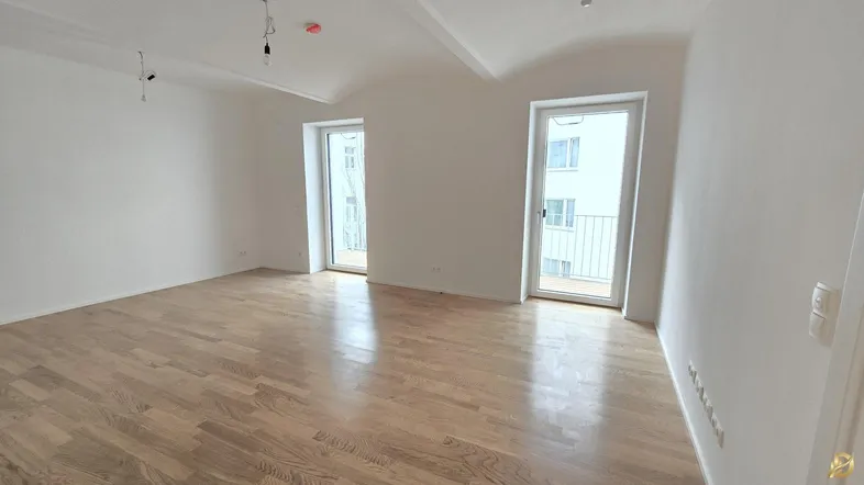 Helles, leeres Zimmer mit Holzboden und zwei französischen Balkonen, bereit zum Einzug.