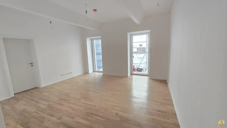 Helles, leeres Zimmer mit neuem Parkettboden und zwei Fenstern, bereit für die Einrichtung.