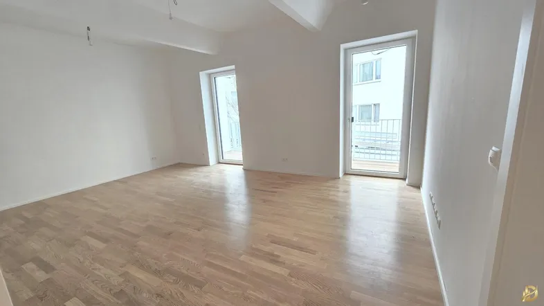 Helles, leeres Zimmer mit Parkettboden und Zugang zu zwei französischen Balkonen.