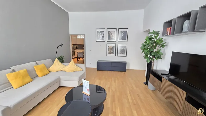 Helles Wohnzimmer mit modernem Sofa, Holzboden und Blick in die angrenzende Küche.