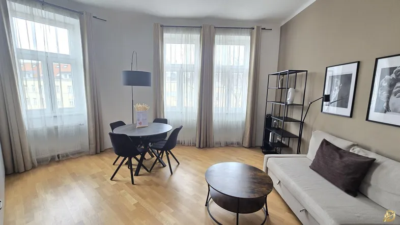 Helles Wohn- und Esszimmer mit Parkettboden, beigem Sofa und modernem Esstisch vor großen Fenstern.