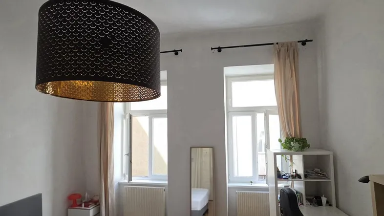 Helles Schlafzimmer mit Holzboden, zwei Fenstern und einem Arbeitsbereich.