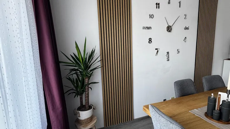 Moderner Essbereich mit Holztisch, bequemen Stühlen und dekorativer Wandgestaltung mit Holzlamellen.