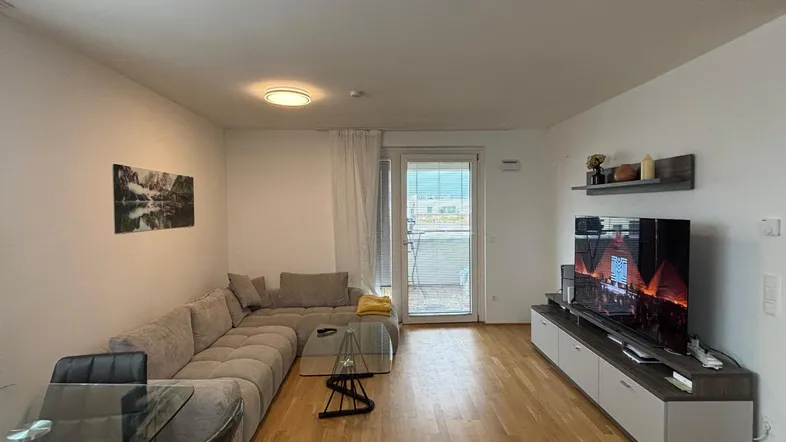Helles Wohn- und Esszimmer mit modernem Sofa, Esstisch und Zugang zum Balkon.