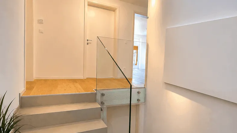 Heller Flur mit moderner Treppe, Glasgeländer und Oberlicht für viel Tageslicht.