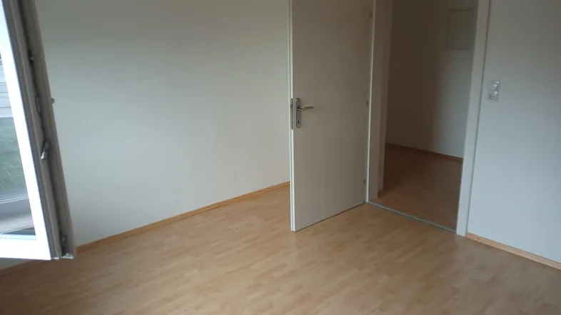 Helles Zimmer mit Laminatboden und einer offenen Tür zu einem weiteren Raum.