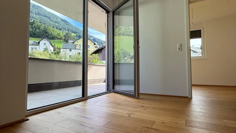 Helles Zimmer mit Holzboden und Zugang zu einem Balkon mit Bergblick.
