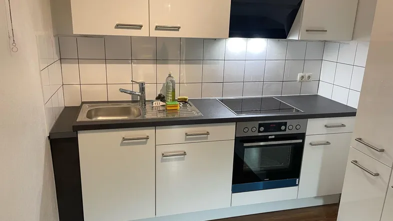 Moderne Einbauküche mit weißen Hochglanzfronten, Kochfeld und Backofen, ideal für kleine Wohnungen.