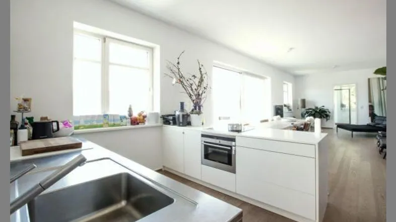 Helle, moderne Küche mit weißen Schränken, integriertem Backofen und Blick in den offenen Wohnbereich.