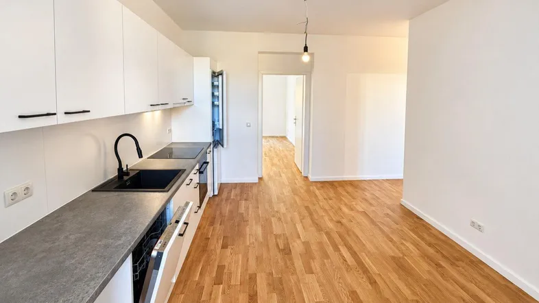 Moderne Einbauküche mit weißen Schränken, dunkler Arbeitsplatte und Holzboden in einem offenen Wohnbereich.