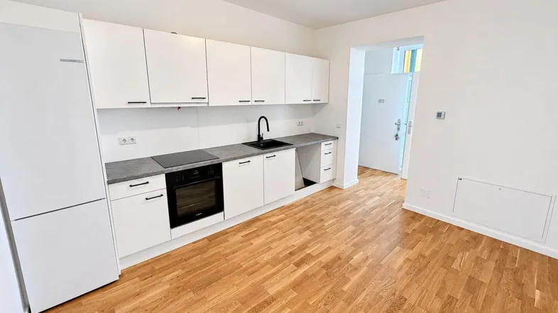 Moderne Einbauküche mit weißen Hochglanzfronten, dunkler Arbeitsplatte und hellem Parkettboden.