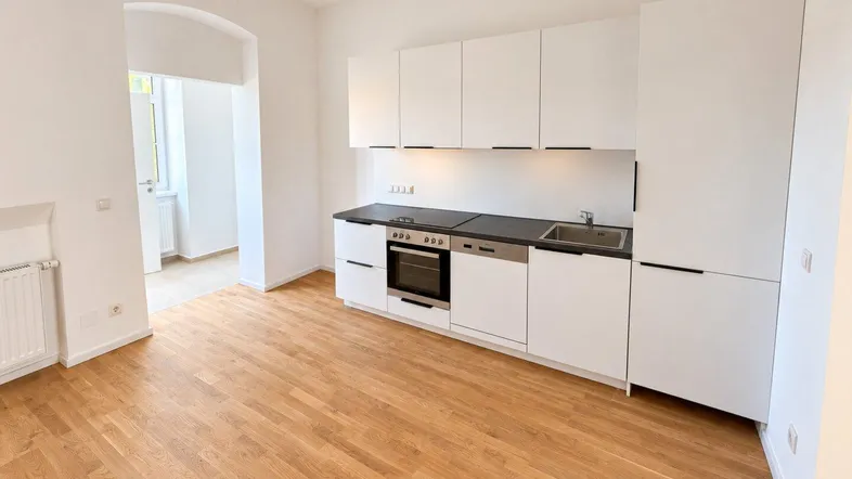 Moderne, offene Einbauküche in Weiß mit dunkler Arbeitsplatte und hellem Holzboden, integriert in den Wohnbereich.