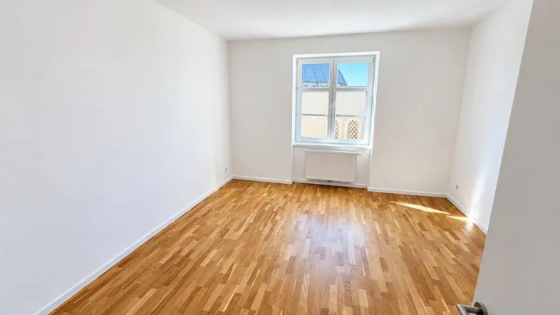 Helles Zimmer mit weißen Wänden und einem schönen Holzparkettboden, bereit zur individuellen Gestaltung.