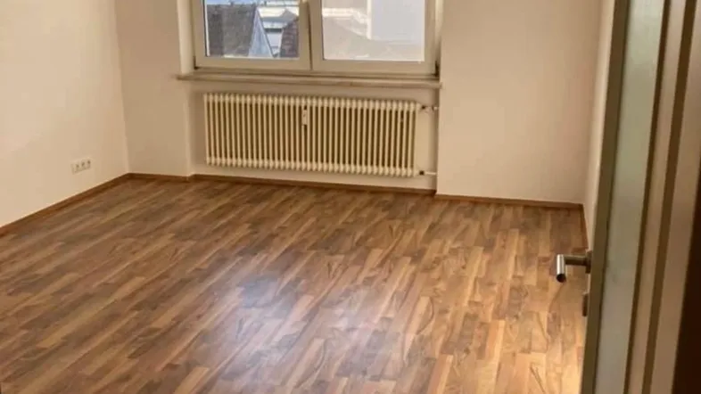 Helles Zimmer mit Laminatboden und Heizkörper unter dem Fenster, bietet einen Blick auf die Umgebung.