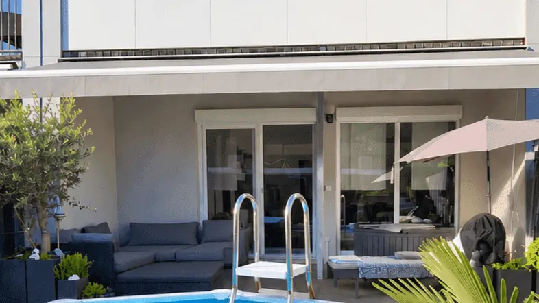 Moderne Terrasse mit Aufstellpool, bequemen Loungemöbeln und Blick auf das Gebäude.