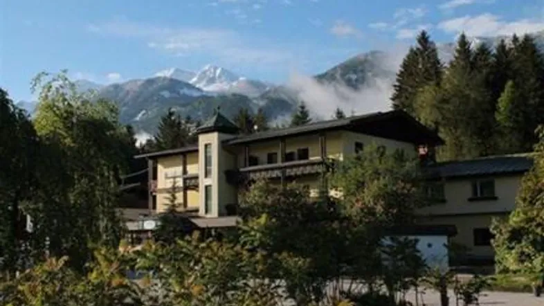 Gebäude mit alpiner Architektur, umgeben von Bäumen und mit beeindruckendem Bergblick auf schneebedeckte Gipfel.