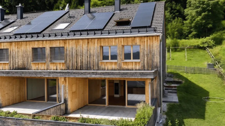 Modernes Reihenhaus mit Holzfassade, Photovoltaikanlage und großzügiger Terrasse im Grünen.