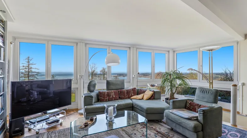Helles Wohnzimmer mit großen Fenstern, die einen weiten Blick auf den See bieten und gemütlichen Sitzgelegenheiten.
