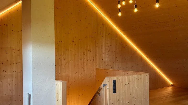 Dachgeschoss mit Holzverkleidung, indirekter Beleuchtung und moderner Hängelampe.