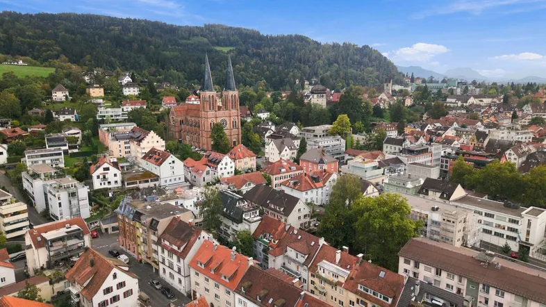 Luftaufnahme einer malerischen Stadt mit historischer Kirche und grünen Hügeln im Hintergrund.