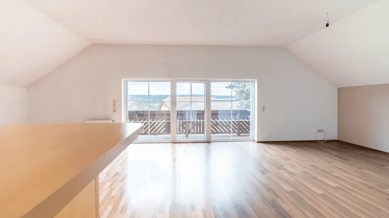 Helles Wohnzimmer im Dachgeschoss mit Holzboden, großen Schiebetüren und Zugang zu einem Balkon mit Weitblick.