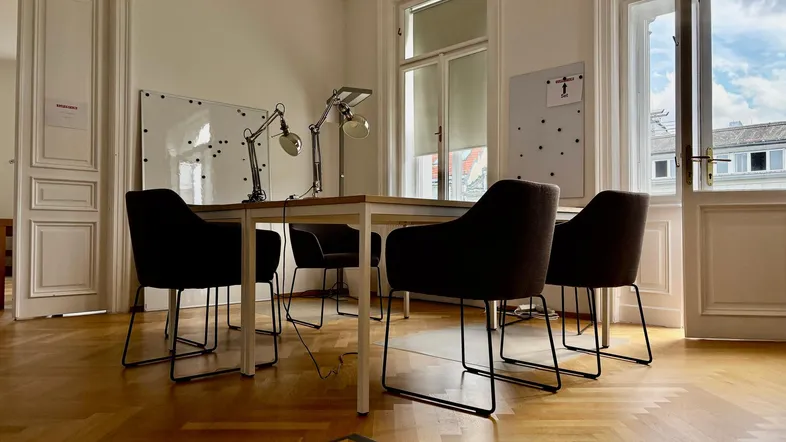 Heller Besprechungsraum mit Holzboden, großen Fenstern und modernen Bürostühlen für produktive Meetings.