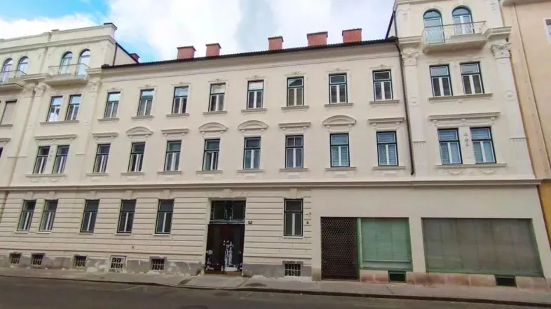 Klassisches Mehrfamilienhaus mit heller Fassade und mehreren Fenstern in städtischer Umgebung.