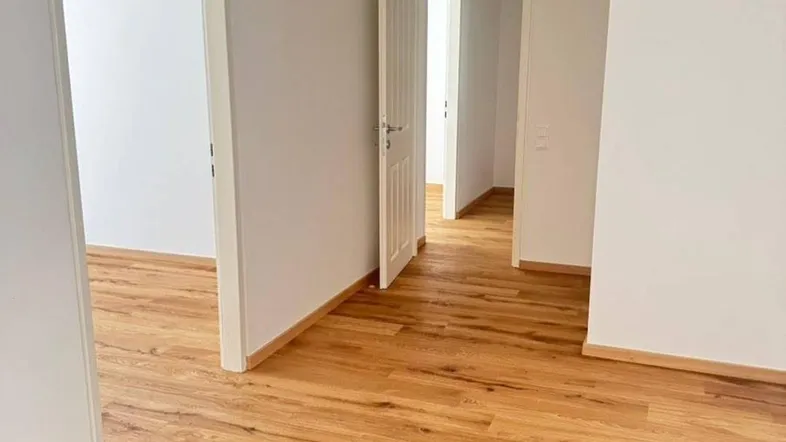 Heller Flur mit neuem Holzparkettboden und weißen Wänden, der zu verschiedenen Räumen führt.