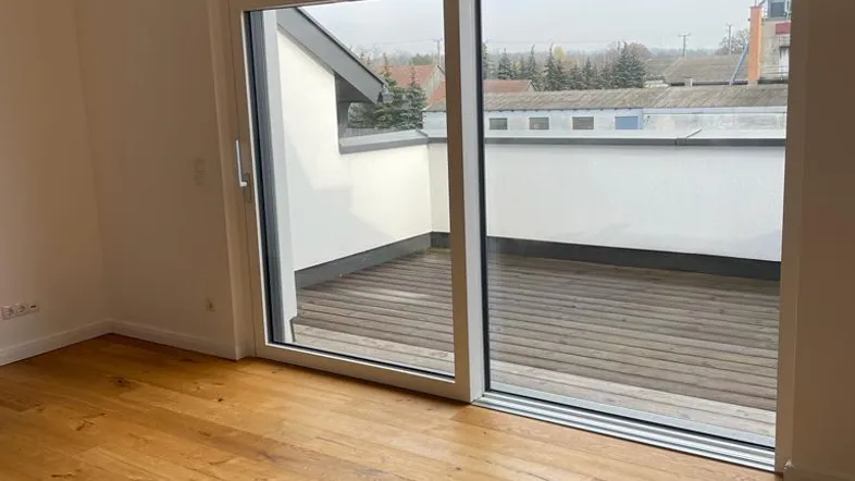 Heller Raum mit Holzboden und großer Schiebetür, die zu einer Holzterrasse führt.