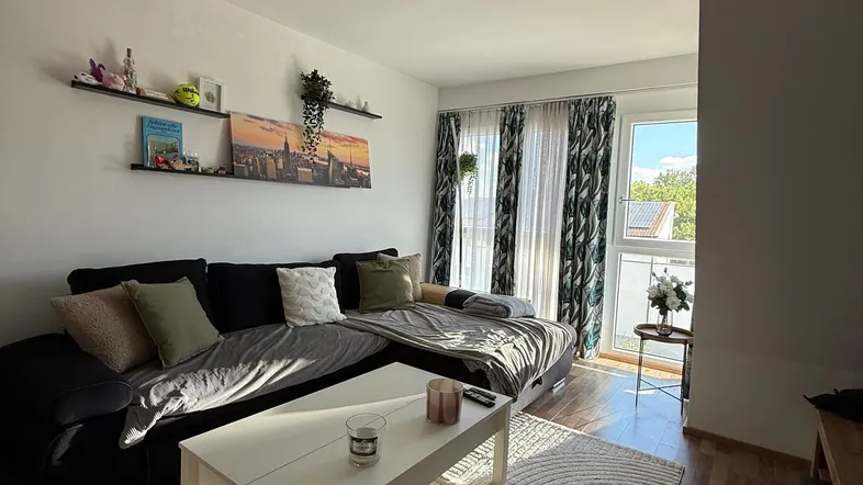 Helles Wohnzimmer mit großem Sofa, Couchtisch und Zugang zu einem Balkon, durchflutet von natürlichem Licht.
