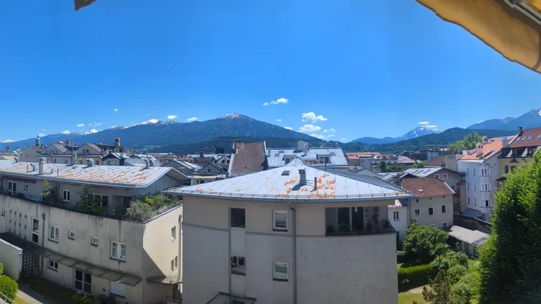 Panoramablick über die Stadt mit schneebedeckten Bergen im Hintergrund von einer sonnigen Terrasse.
