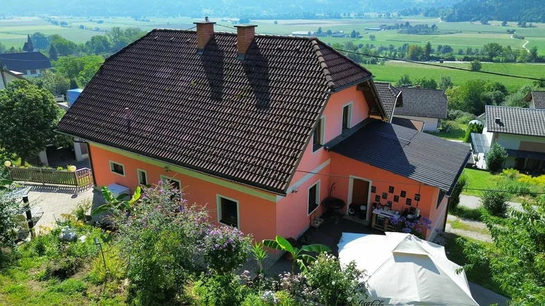Haus mit Ziegeldach und Gartenbereich, umgeben von grüner Landschaft und Hügeln.