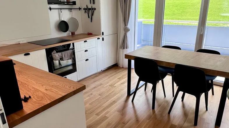 Helle Küche mit Holzarbeitsplatten, Essbereich und großen Fenstern mit Blick ins Grüne.