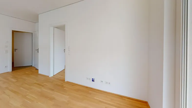 Helles, leeres Zimmer mit Parkettboden und weißen Wänden, bereit zum Einzug.