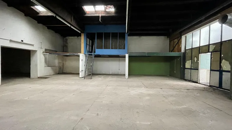 Großer, leerer Lagerraum mit Betonboden, hohen Decken und einer blauen Mezzanine-Struktur.