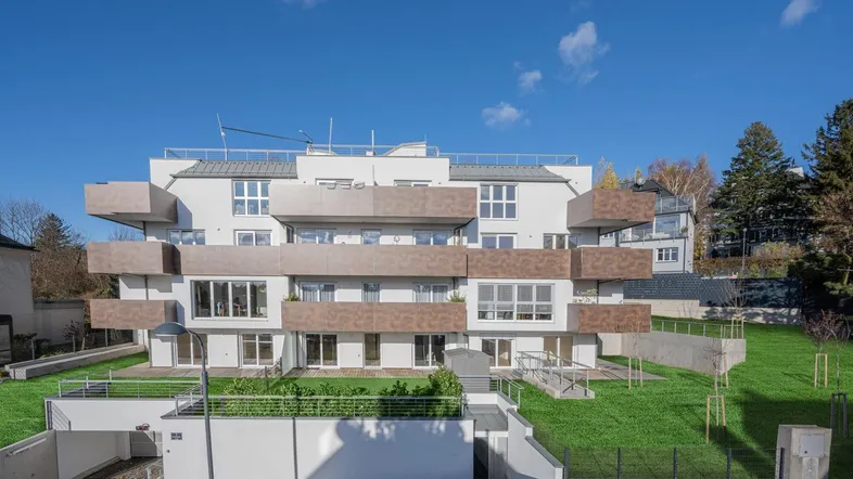 Moderne Wohnanlage mit mehreren Balkonen und Grünflächen unter blauem Himmel.