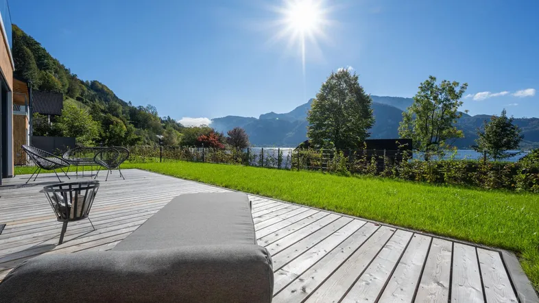 Große Holzterrasse mit Liegestuhl und atemberaubendem Blick auf den See und die umliegenden Berge.