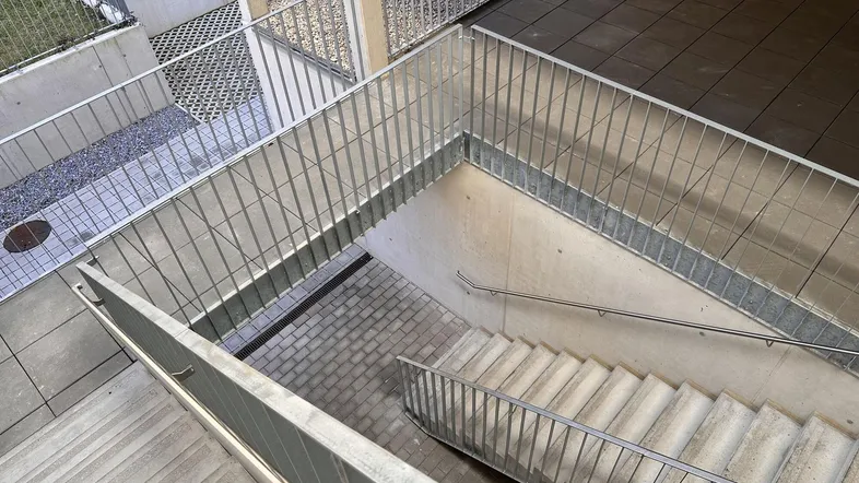 Außenbereich mit Betontreppe und Metallgeländer, der zu den unteren Ebenen führt.