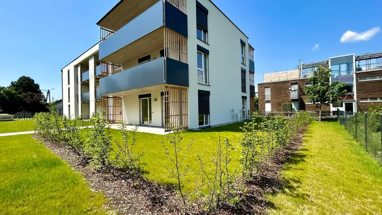 Modernes Mehrfamilienhaus mit Balkonen und gepflegter Grünfläche unter blauem Himmel.
