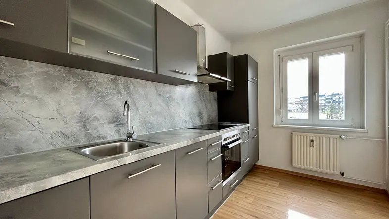 Moderne Küche mit grauen Schränken, integrierten Geräten und einem Fenster für natürliches Licht.