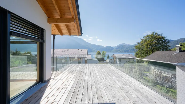 Große Holzterrasse mit Glasgeländer und atemberaubendem Blick auf den See und die umliegenden Berge.