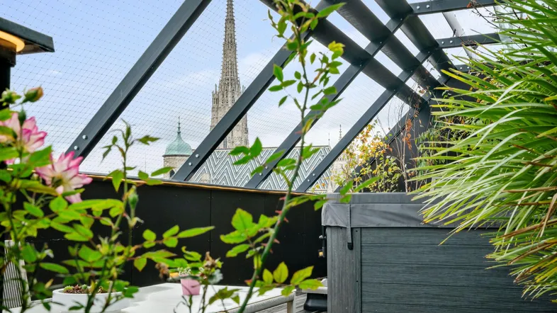 Dachterrasse mit Whirlpool, Pflanzen und Blick auf eine historische Kirchturmspitze.