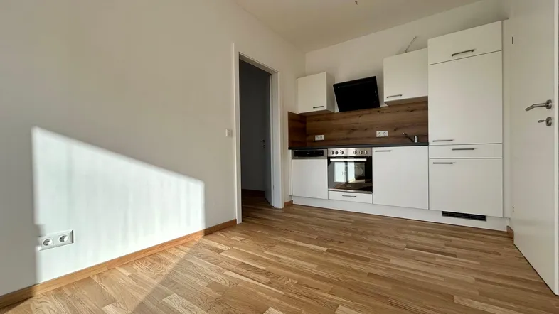 Helle, offene Küche mit weißen Schränken, Holzakzenten und Parkettboden in einem modernen Wohnraum.